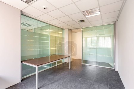 In einem bankrotten Bürogebäude ist einer der vielen leeren Räume mit transparenten, massiven Glaswänden und einer veralteten Deckenverkleidung reparatur- und sanierungsbedürftig
