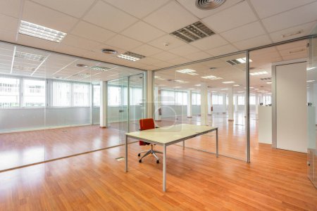 In a bankrupt office building, one of the many empty rooms with transparent, solid glass wall panels and an outdated ceiling covering is in need of repair and refurbishment