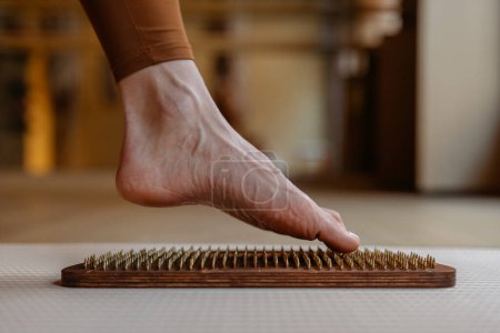 Los contornos de un pie explorando la aguda sensación de las clavijas de madera en una tabla de acupresión.