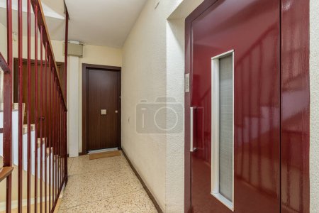 Foto de Un plano interior de un vestíbulo de un edificio residencial con una puerta roja clásica y suelos de terrazo. - Imagen libre de derechos