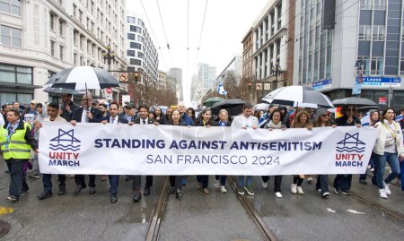 Téléchargez les photos : San Francisco, CA - 03 mars 2024 : Des politiciens et des participants non identifiés à une marche contre l'antisémitisme qui monte Market Street jusqu'au Civic Center. Marcher sous la pluie. - en image libre de droit
