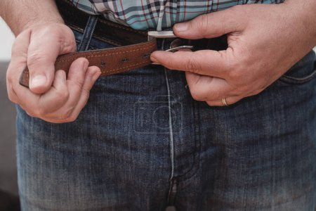Close-up of a man's hands putting on a pair of jeans and adjusting the belt.