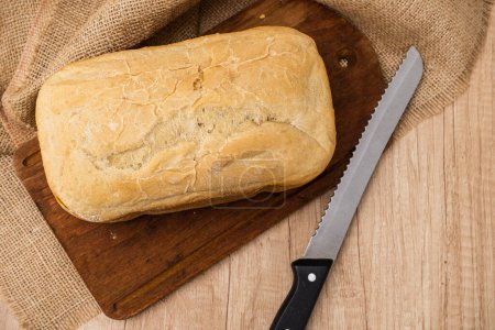 Draufsicht auf ein hausgemachtes Brot, das mit einer Brotmaschine auf einem Holzbrett mit einem Brotmesser zubereitet wird. Raum für Text.