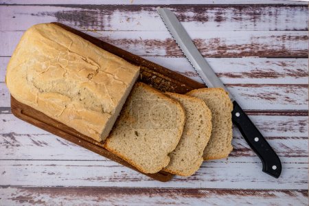 Photo for Aereal view of a bread last made with a home bread machine with freshly cut slices on a wooden board next to the bread knife. - Royalty Free Image