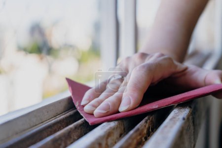 Téléchargez les photos : Normal view of a woman's hands sanding a window frame before painting. Empowered woman concept. Landscape orientation - en image libre de droit