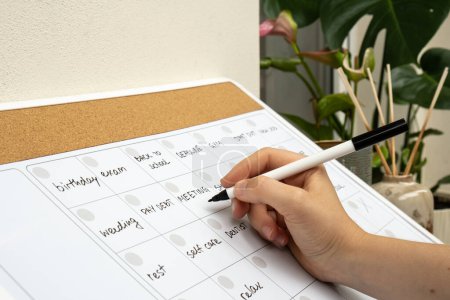 Photo for Female hand writing with marker on Monthly PLANNER filled with appointments and plans for next month. Busy month schedule. Magnetic board with the days of the month. Place to enter important matters - Royalty Free Image