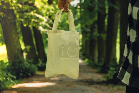 Close-up of Unrecognizable female hand holding cotton eco bag in park. Reusable eco bag in park. Mock up Sustainable lifestyle. Plastic free zero waste free living. Go green Environment protection