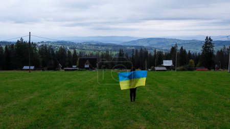 Photo for Woman with Ukrainian national flag waving Patriotism Aerial view of Zakopane town underneath Tatra Mountains taken from the Gubalowka mountain range. Drone High mountains and green hills in summer or - Royalty Free Image