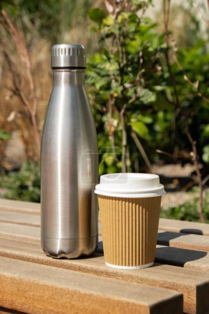 Reusable steel thermo water bottle on wooden bench with paper cup. Sustainable lifestyle. Plastic free zero waste free living. Go green Environment protection. Health-conscious. Steel thermo water