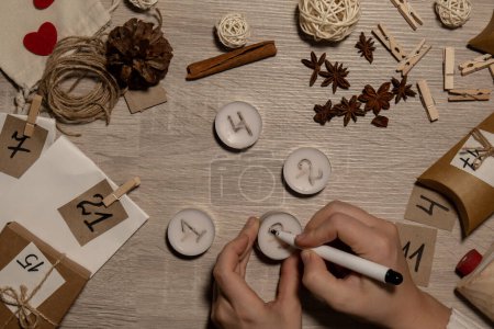 Téléchargez les photos : Unrecognizable young woman paint numbers on tea candles. Female making homemade advent calendar Made with your own hands step by step DIY crafts do it yourself. Preparation to christmas concept - en image libre de droit