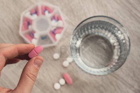 Photo for Woman sorting pills Organizer weekly shots Closeup of medical pill box with doses of tablets for daily take medicine with white pink drugs and capsules. Young woman getting her daily vitamins at home - Royalty Free Image