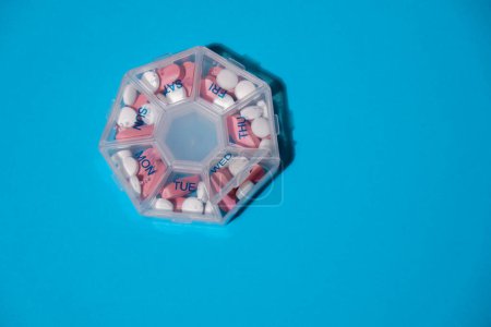 Photo for Organizer weekly shots on blue background with Copy space for your text. Closeup of medical pill box with doses of tablets for daily take medicine with white pink drugs and capsules. Daily vitamins at - Royalty Free Image