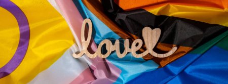 Téléchargez les photos : Banner Wooden word love with heart romance on Rainbow LGBTQIA flag made from silk material. Valentines Day greeting card. Symbol of LGBTQ pride month. Equal rights. Peace and freedom. Support LGBTQIA - en image libre de droit