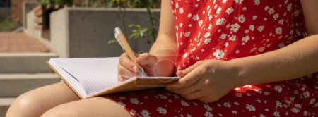 Unrecognizable Young woman in red dress Writing Gratitude Journal on wooden bench. Today I am grateful for. Self discovery journal, self reflection creative writing, self growth personal development