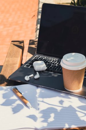 Take away coffee in craft recycling paper cup with paper notebook laptop with wireless headphones. Mockup Coffee break. Audio healing, sound therapy wellness rituals, positive mental health habits