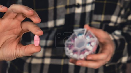 Photo for Female hands sorting pills Organizer weekly shots Closeup of medical pill box with doses of tablets for daily take medicine with white pink drugs and capsules. Young woman getting her daily vitamins - Royalty Free Image