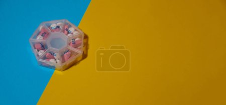 Photo for Organizer weekly shots medical pill box with doses of tablets for daily take medicine with white pink drugs and capsules. Copy space Daily vitamins at home. Medication dietary supplements, immunity - Royalty Free Image