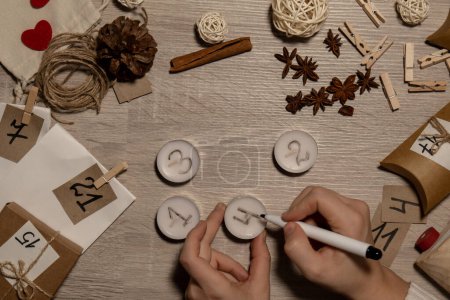 Téléchargez les photos : Unrecognizable young woman paint numbers on tea candles. Female making homemade advent calendar Made with your own hands step by step DIY crafts do it yourself. Preparation to christmas concept - en image libre de droit