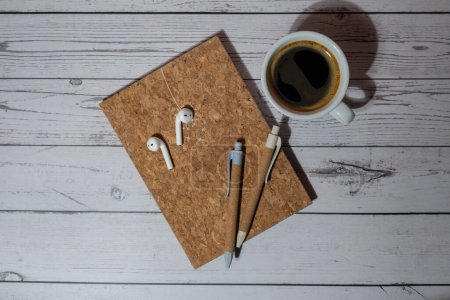Top view, wooden Office desk with cup of coffee, eco pen, wireless headphones and recycle notebook. Business or student workspace concept Flat lay. Personal diary Audio healing, sound mental health