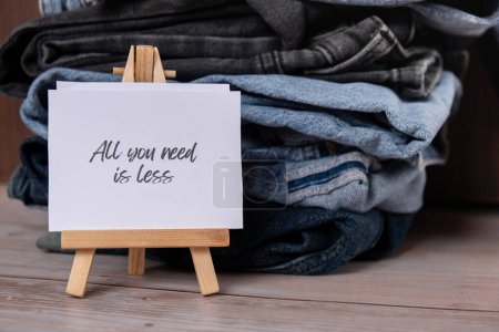 ALL YOU NEED IS LESS text on paper note on Jeans clothes assortment Second hand sustainable shopping. Capsule minimal wardrobe. Sustainable fashion overconsumption, conscious buying consumption, slow