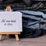 ALL YOU NEED IS LESS text on paper note on Jeans clothes assortment Second hand sustainable shopping. Capsule minimal wardrobe. Sustainable fashion overconsumption, conscious buying consumption, slow