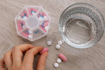 Photo for Woman sorting pills Organizer weekly shots Closeup of medical pill box with doses of tablets for daily take medicine with white pink drugs and capsules. Young woman getting her daily vitamins at home - Royalty Free Image