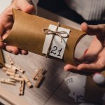 Unrecognizable young woman sticks number on craft bag, fastens with clothespin. Female making kraft paper for homemade advent calendar Made with your own hands step by step DIY crafts do it yourself