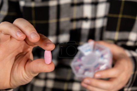 Foto de Píldoras de clasificación de manos femeninas Organizador inyecciones semanales Primer plano de la caja de pastillas médicas con dosis de tabletas para tomar diariamente medicamentos con drogas y cápsulas de color rosa blanco. Mujer joven recibiendo sus vitaminas diarias - Imagen libre de derechos