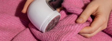 Photo for Woman using Anti-pilling razor at home. Device for shaving clothes. Anti-Plush fabric Shaver. Electric portable sweater pill defuzzer Lint remover from pink acrylic or wool sweater. Slow fashion - Royalty Free Image