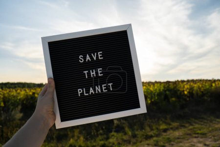 Personne méconnaissable avec un message de bannière Enregistrer la planète dans le champ de tournesol le jour ensoleillé. Signez le Jour de la Terre. Concept d'écologie et d'éco-activisme questions environnementales Arrêter le réchauffement climatique. Allez vert