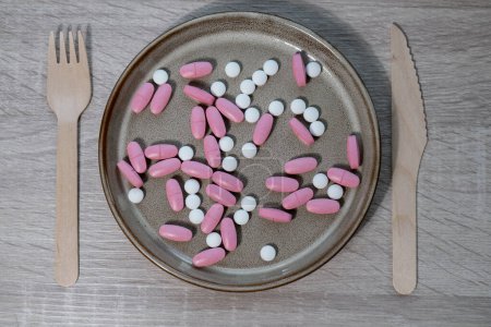 Téléchargez les photos : Organizer weekly shots with fork and knife medical pill box with doses of tablets for daily take medicine with white pink drugs and capsules. Daily vitamins at home. Medication dietary supplements - en image libre de droit
