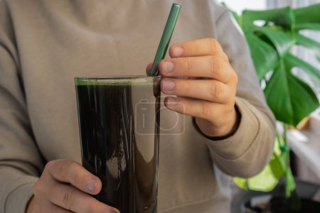 Eine unkenntliche Frau trinkt ein natürliches Bio-Pulver aus grünen Spirulina-Algen auf neutralem beigem Hintergrund. Chlorella Algen vegane Superfood Cocktails Smoothie Ergänzung Quelle und Entgiftungsgetränk