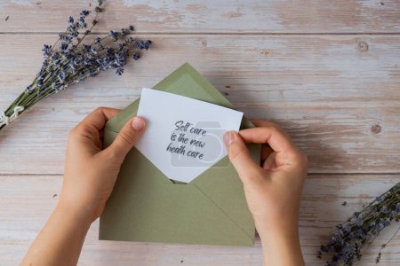 SELF CARE IS THE NEW HEALTH CARE text on supportive message paper note reminder from green envelope. Flat lay composition dry lavender flowers. Concept of inner happiness, slowing-down digital detox