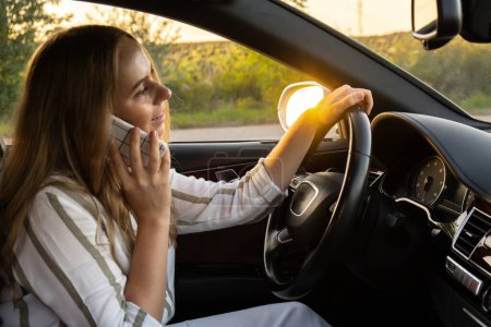 Mujer joven y feliz hablando por teléfono móvil mientras conduce el coche. Mujer de negocios hablando de llamadas telefónicas en automóvil. Conducción insegura y arriesgada. Concepto de multitarea 