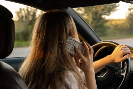 Glückliche junge Frau, die während der Autofahrt mit dem Handy spricht. Geschäftsfrau telefoniert im Auto. Unsicher riskantes Fahren. Konzept des Multitasking 