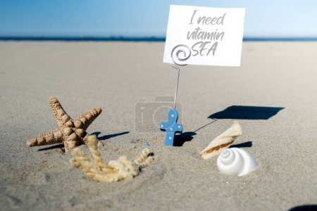 I NEED VITAMIN SEA text on paper greeting card in anchor paper holder and starfish seashell summer vacation decor. Sandy beach sun coast. Holiday concept postcard. Getting away Travel Business concept