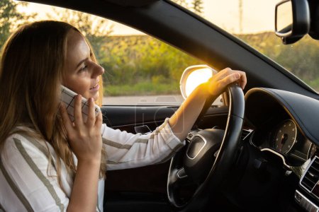 Mujer joven usando el teléfono móvil mientras conduce un coche en la carretera durante el atardecer. Womandriver tiene accidente llamando con el teléfono inteligente para obtener ayuda. Mujer de negocios ocupado concepto de conducción
