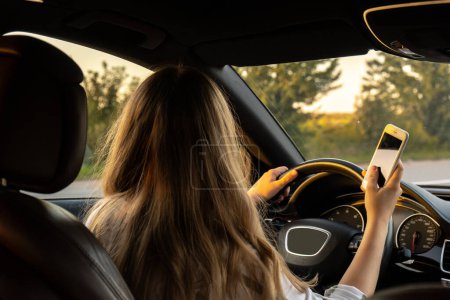 Jeune femme utilisant un téléphone portable tout en conduisant une voiture sur la route pendant le coucher du soleil. Womandriver a un appel d'accident avec smartphone pour de l'aide. Femme d'affaires concept de conduite occupé