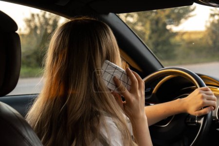 Happy young woman speaking by mobile phone while driving car. Business woman talking phone call in automobile. Unsafely risky driving. Concept of multitasking 