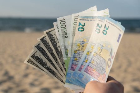 Unrecognizable woman Displaying Spread of Cash euros and dollars bills on sandy beach coastline. Concept finance saving money for holiday vacation. Costs in travel holidays. Extra money, passive