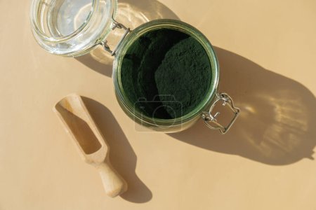 Organic blue-green algae spirulina powder food in glass jar with wooden spoon. Top view flat lay. Health benefits of spirulina chlorella. Dietary supplement superfood concept