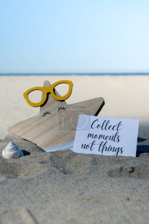 COLLECT MOMENTS NOT THINGS text on paper greeting card on background of funny starfish in glasses summer vacation decor. Sandy beach sun coast. Slowing-down, enjoying the moment, good moments, slow