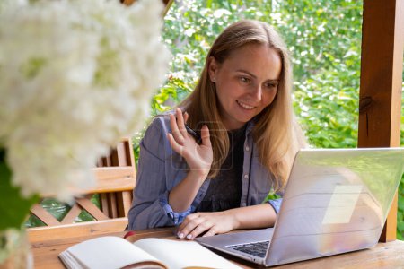 Junge Freiberuflerin arbeitet online mit Laptop und genießt die schöne Natur im Garten. Online-Treffen Bildung. Arbeit, Arbeit aus dem Urlaub, hybrides Arbeitsmodell