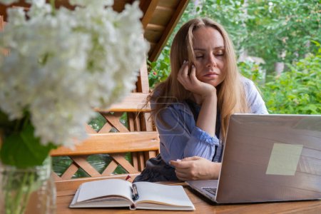 Upset sleepy Female student has online lesson education outdoor in garden wooden alcove. Blonde woman sitting outside work on laptop having video call. Unity with nature