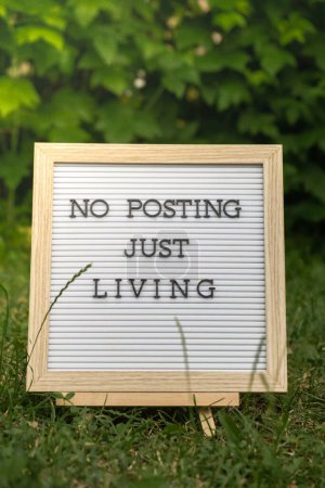 Letter board with text NO POSTING JUST LIVING in grass green background. Concept of digital detox, unplugging from technology break. Mindful living without gadgets 