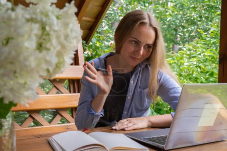 Photo for Young happy woman focuses on her laptop in wooden alcove. Relaxed outdoor setting emphasizes comfort and productivity. Remote work learning concept - Royalty Free Image