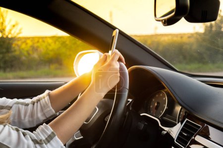 Young woman using mobile phone while driving car on highway road during sunset. Womandriver has accident calling with smartphone for help. Business woman busy driving concept