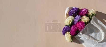 Mixed colorful flowers in cotton bag. Creative minimalistic flowers. Concept of holiday celebrating present and gift. Bouquet delivery Copy space