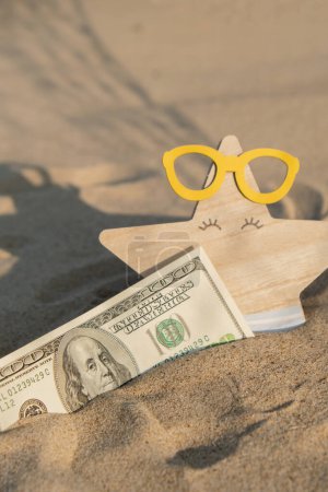 Money american hundred dollar bills in sandy beach with starfish. Concept finance saving money for holiday vacation. Costs in travel holidays. Shadows