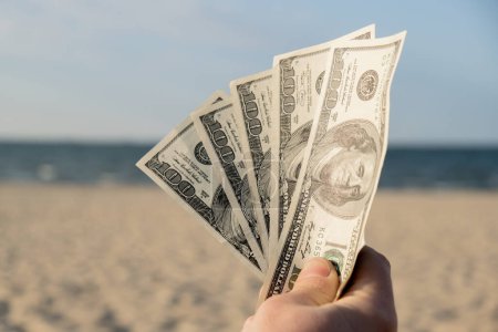 Photo for Unrecognizable woman Displaying Spread of Cash dollars bills on sandy beach coastline. Concept finance saving money for holiday vacation. Costs in travel holidays. Extra money, passive income - Royalty Free Image